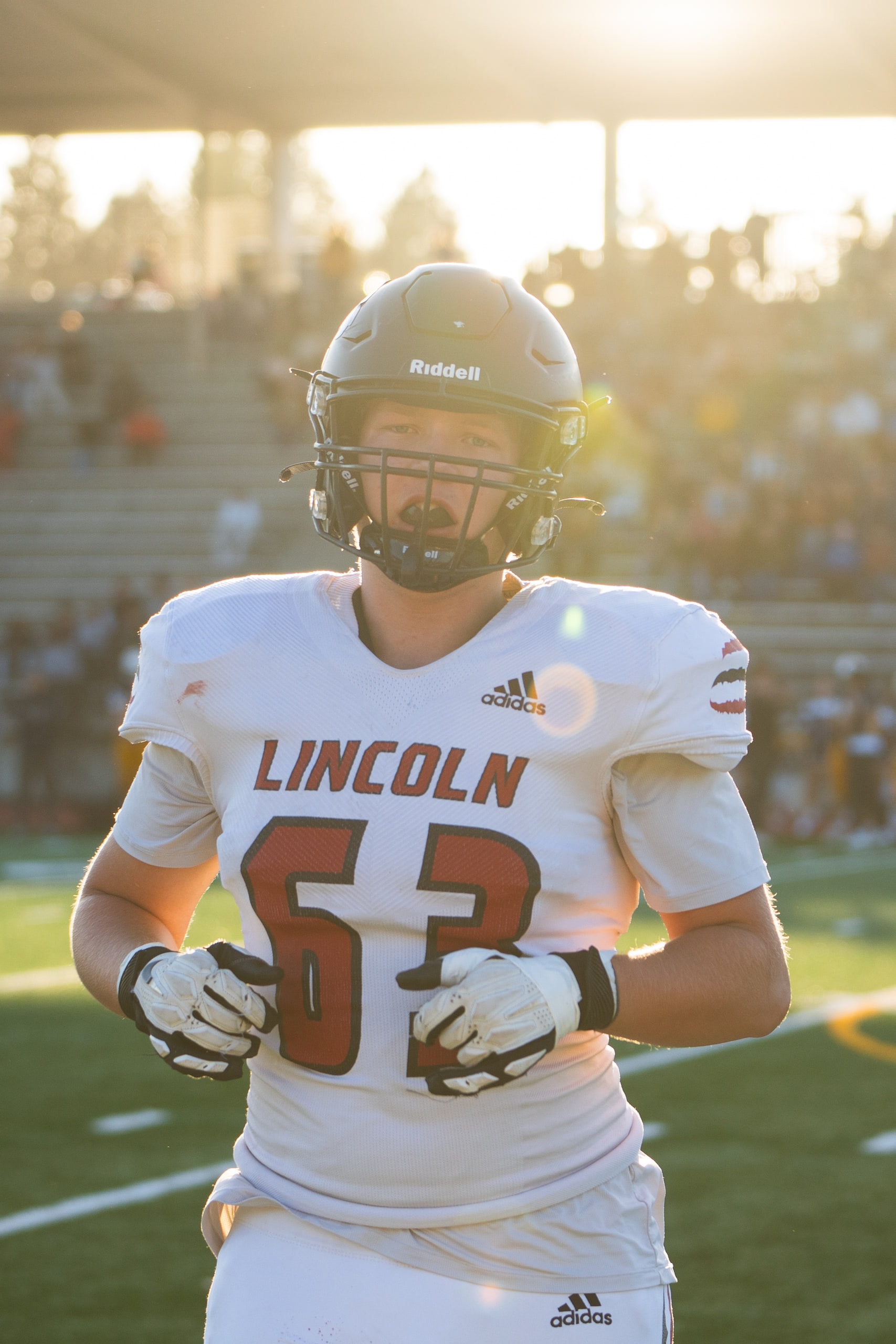 A player in a white number 63 jersey backlit by low sun