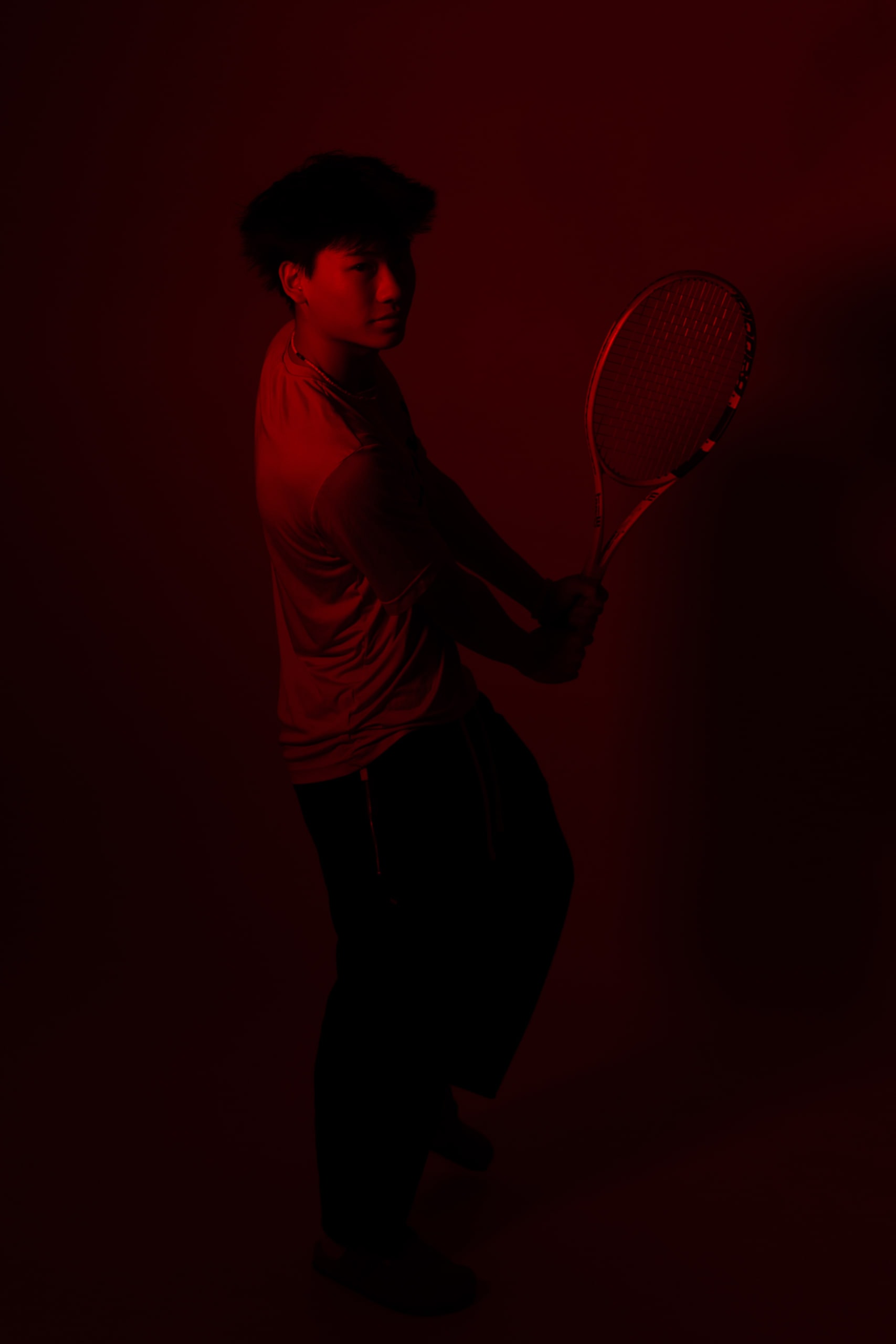 A tennis player in profile lit in deep red